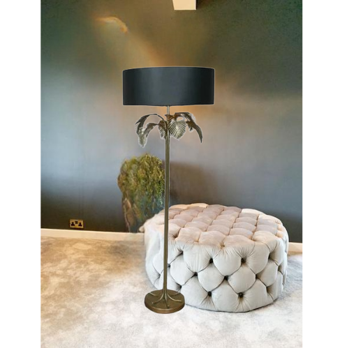 Decorative floor lamp with black shade and palm leaf design next to a tufted ottoman.