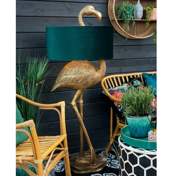 Decorative flamingo lamp with a teal shade in an outdoor setting with chairs and plants.